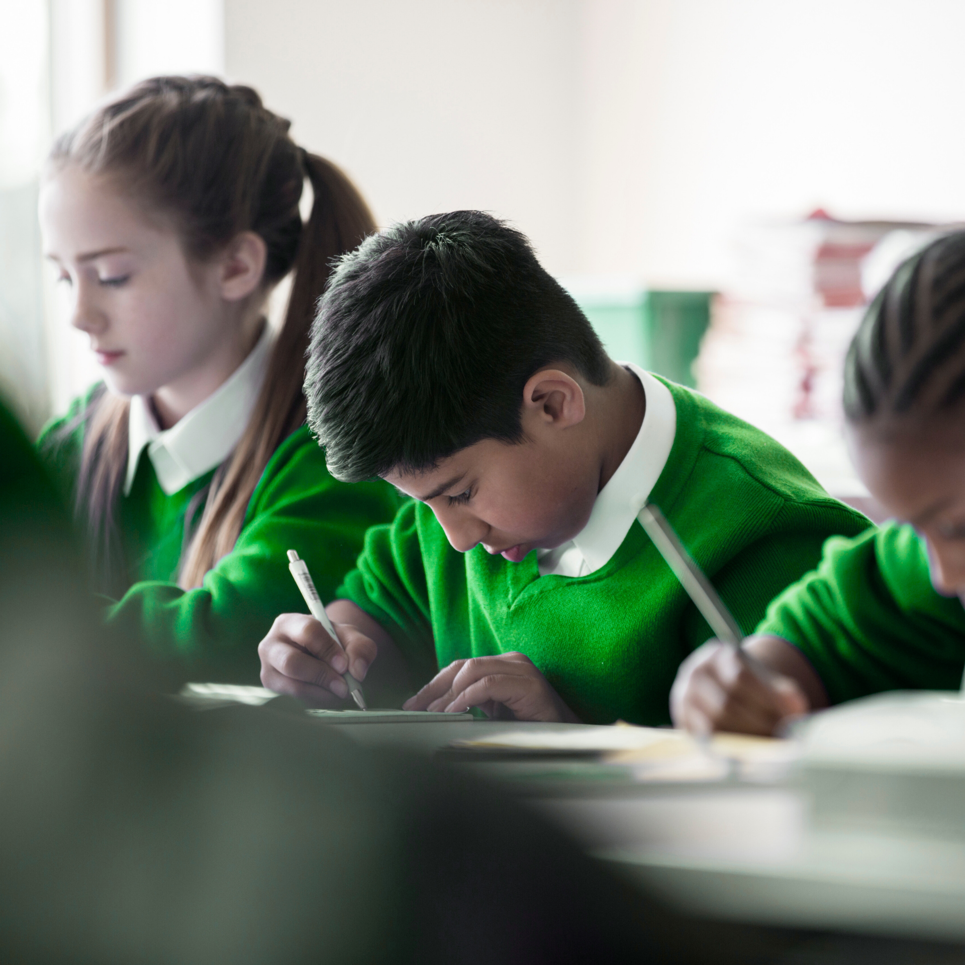 Primary pupils writing at a desk in a classroom
