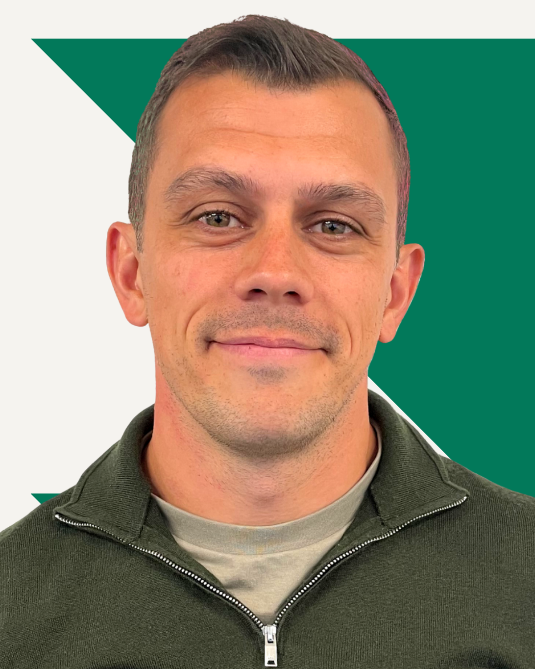 Myles Jackson smiling, wearing a green zip-up sweater, in front of a red geometric pattern.