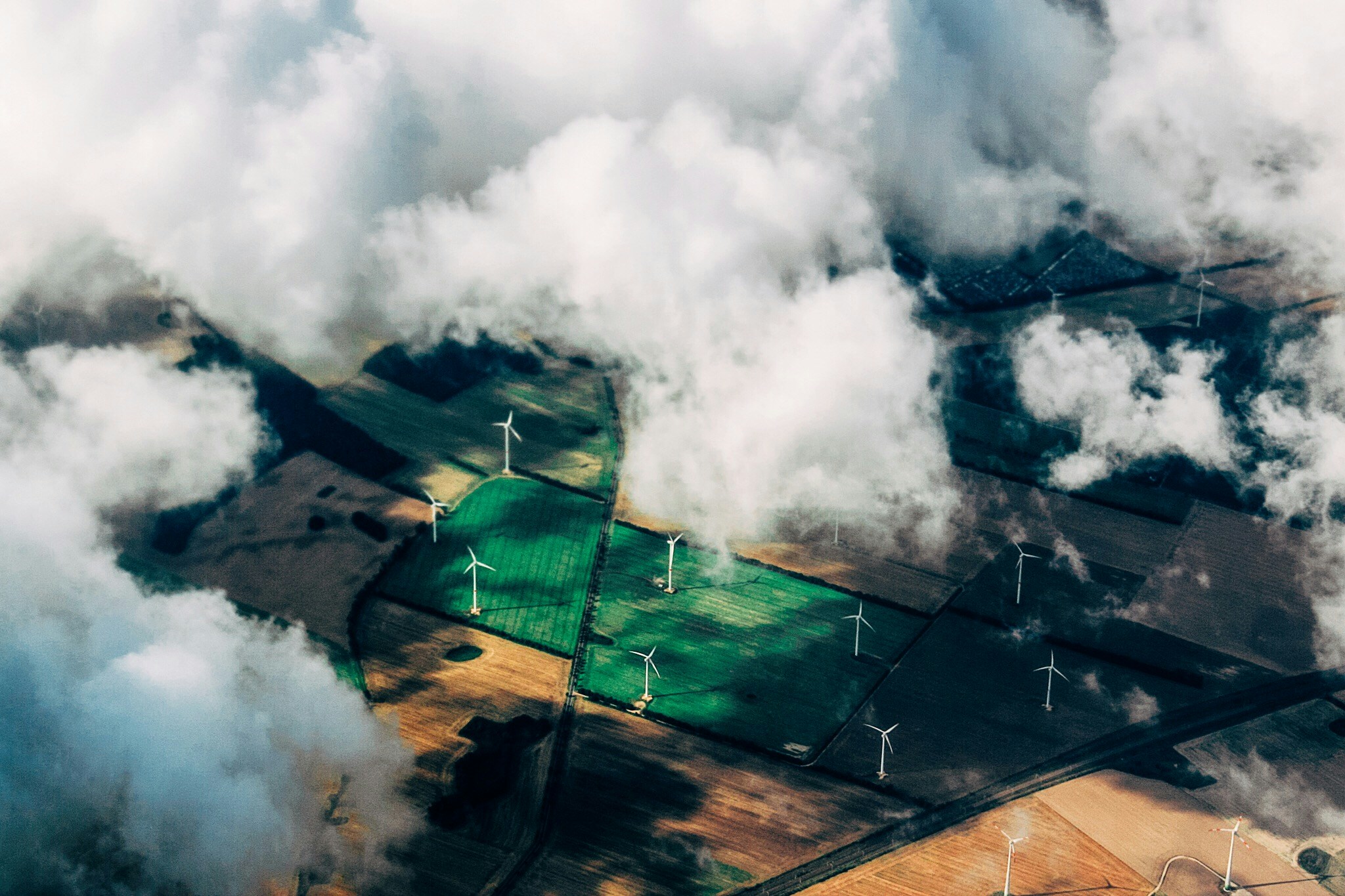 Aerial view of wind turbines across green and brown farmland, partially covered by clouds