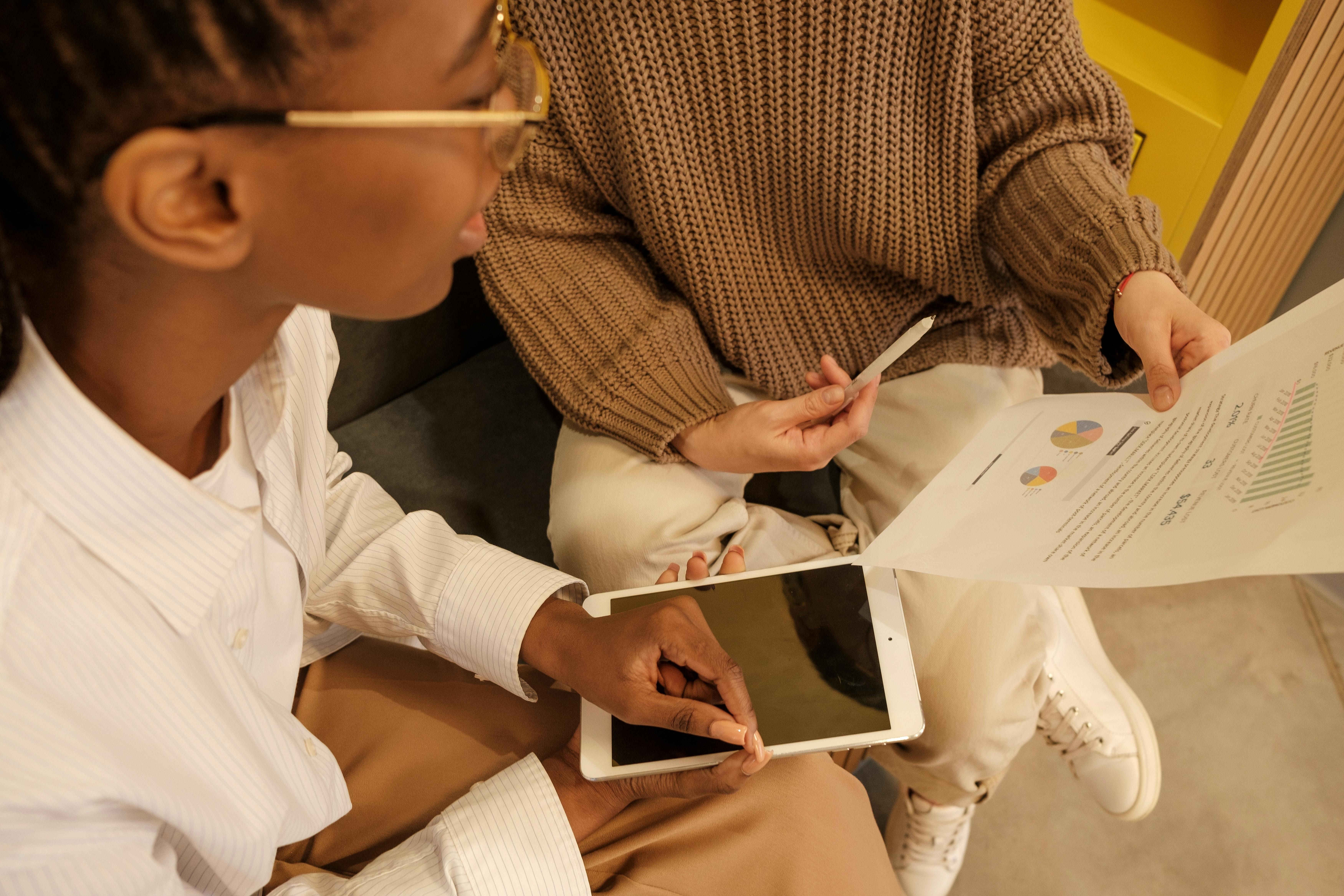 Two employees talking over data and insights using a document and a tablet device.