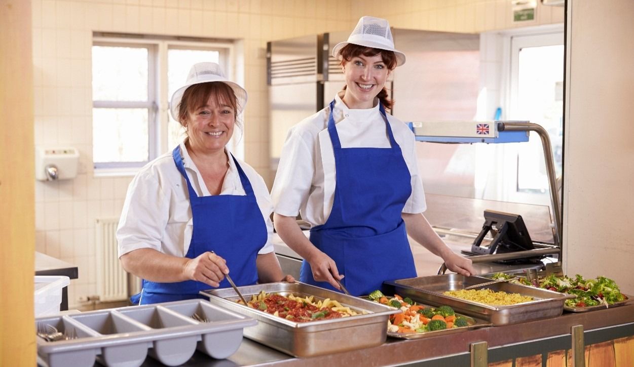Workers smiling serving food in school cafeteria