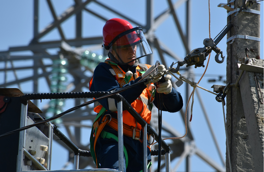 Electrical technician carrying out power line maintenance using safety equipment at a utility substation.