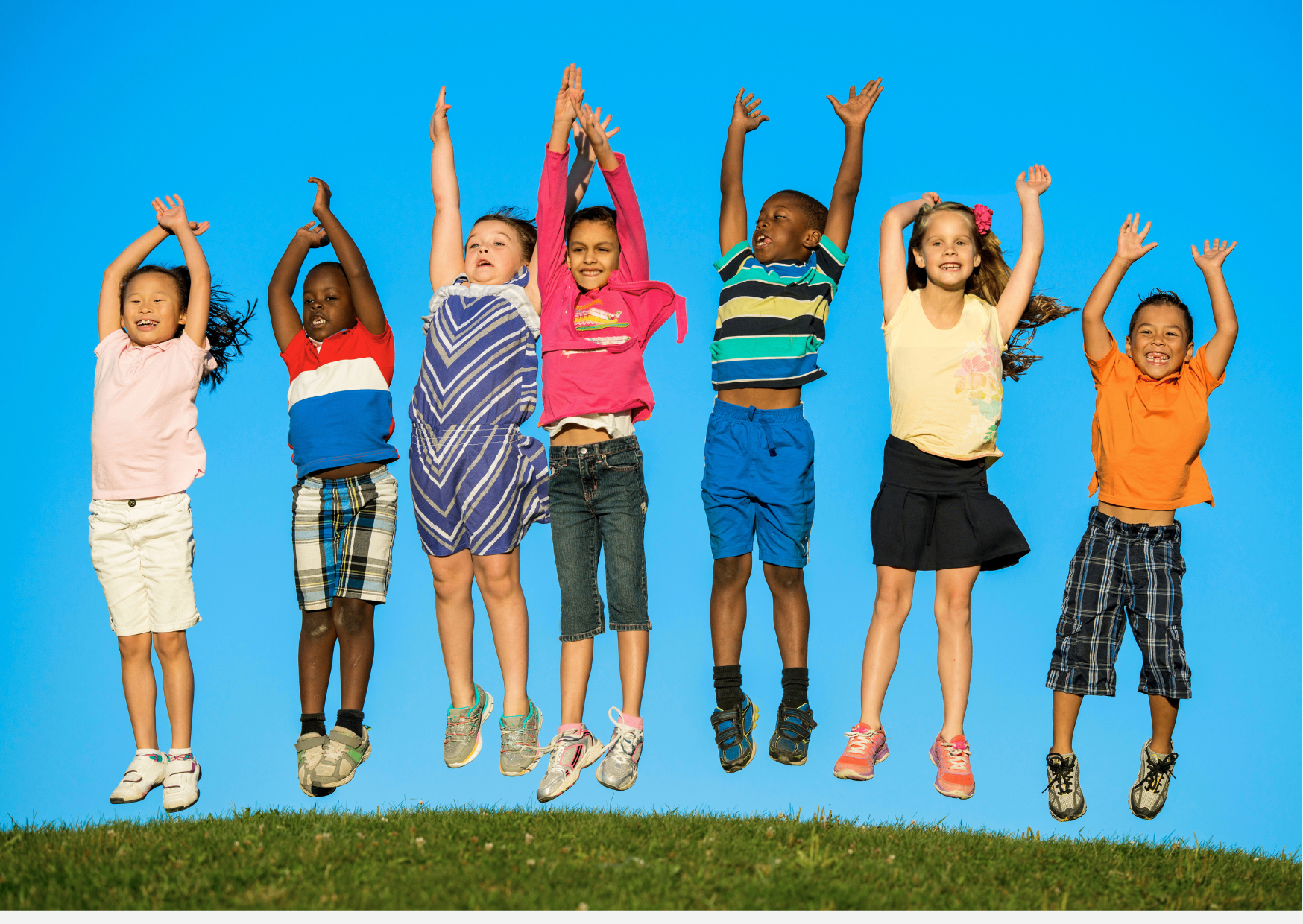 Children jumping on some grass with a bright blue sky in the background