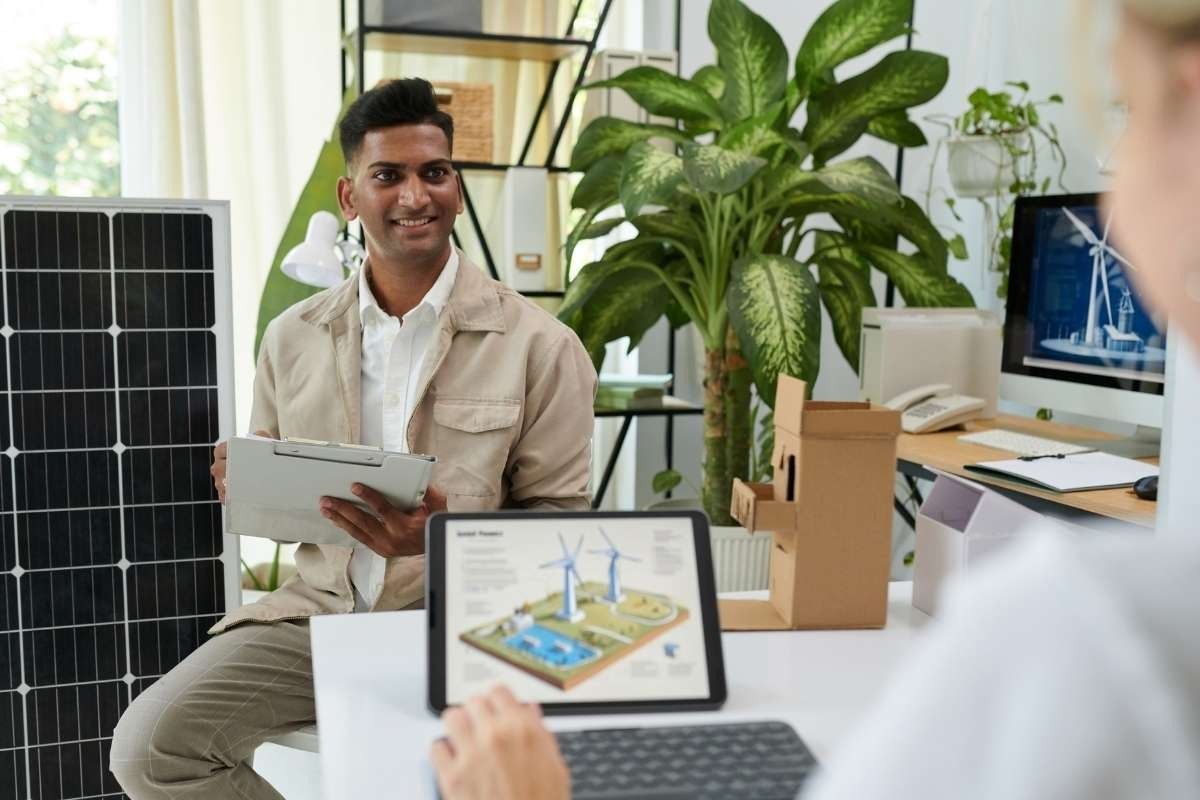 Man sitting whilst holding a tablet smiling at a person sitting oppostie