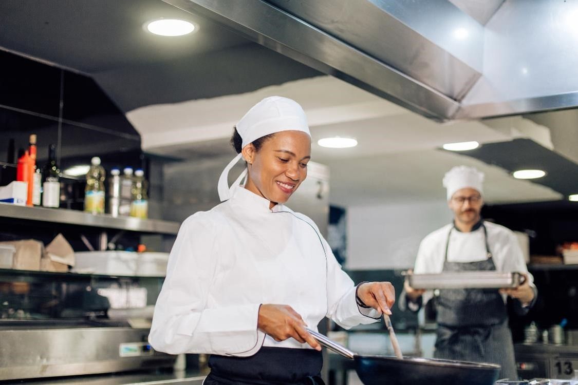 A smiling commis chef cooking in a kitchen