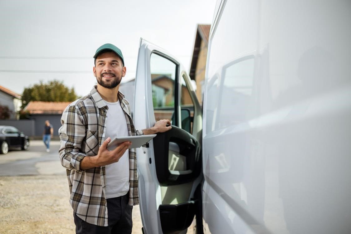 A drivers mate holding a tablet near a van 