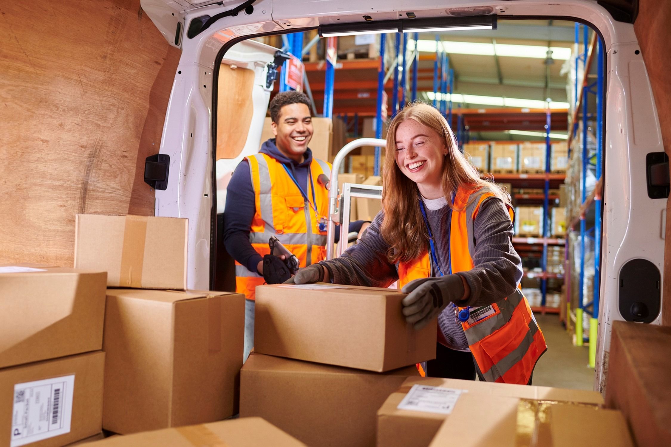 Two people in hi-vis vests smiling and packing boxes into a van