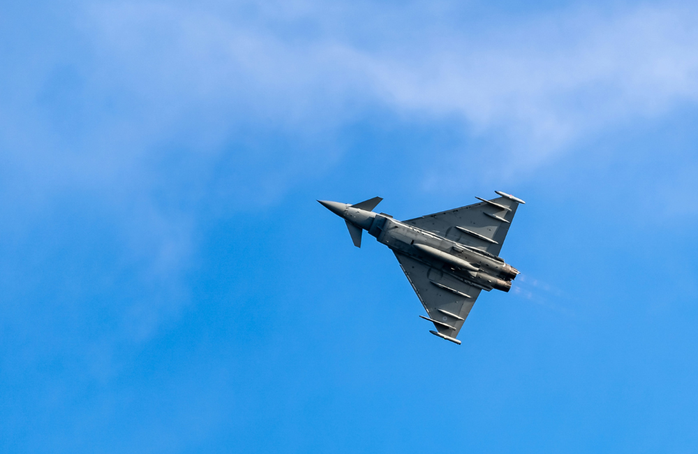Single military fighter jet banking through a blue sky with light cloud cover in the background
