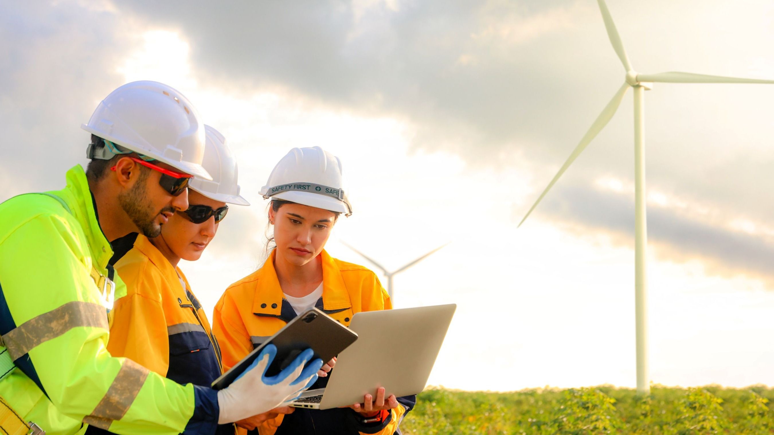 Male and female engineers team walk together wind farm standing tall against cloudy sky sharing ideas about renewable energy from the earth reviewing plans and collecting data on completed 