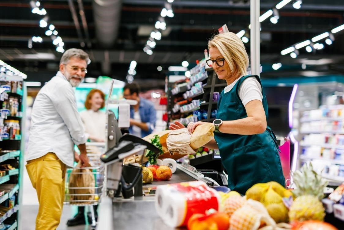 A cashier in a green apron scanning items at a grocery store