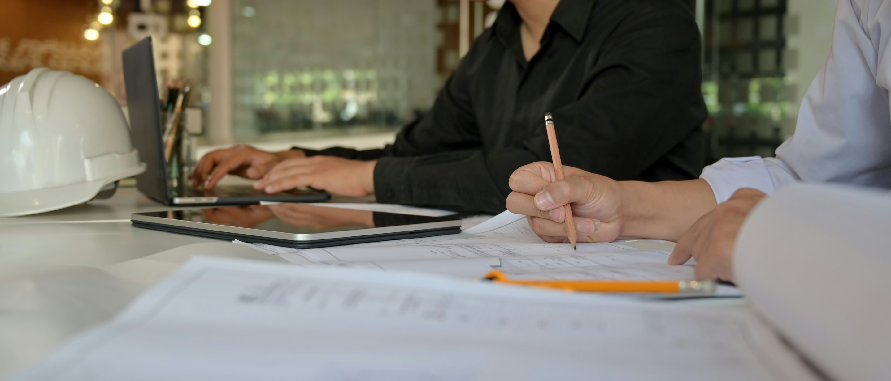 Two people writing at a desk with a laptop