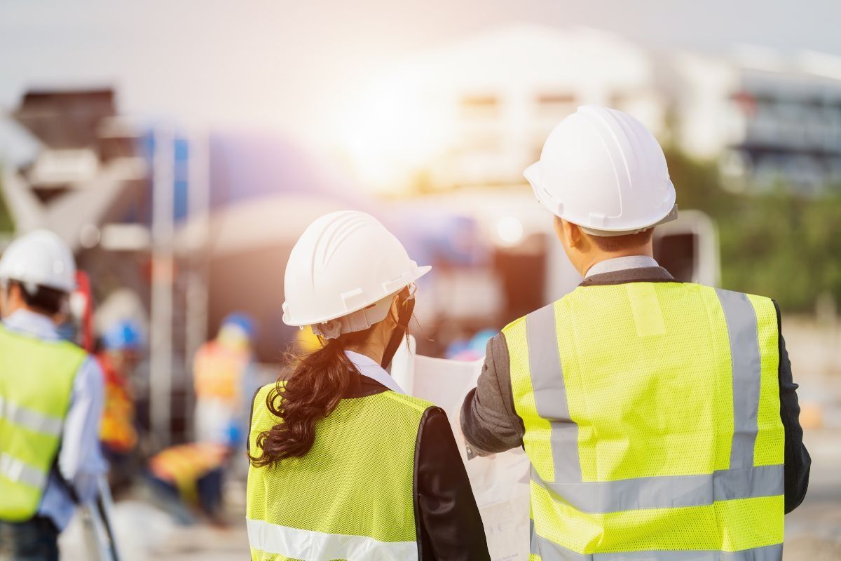 Two people in hard hats and bright coloured safety vests at a construction site
