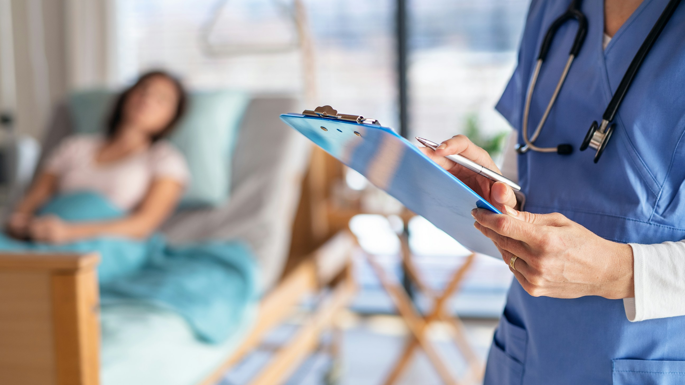 A nurse writing on their clipboard with a patient in the background