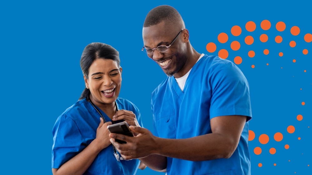 Two healthcare professionals in blue scrubs looking at a mobile phone