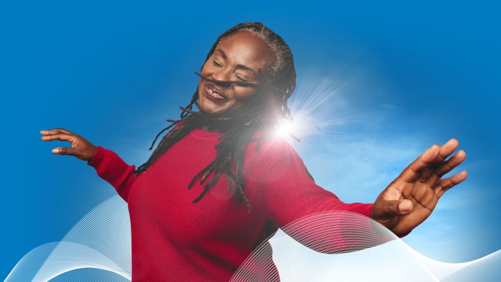Doctor standing outdoors with arms open against a bright blue sky, symbolising wellbeing, freedom and positive energy for doctors in Ireland.