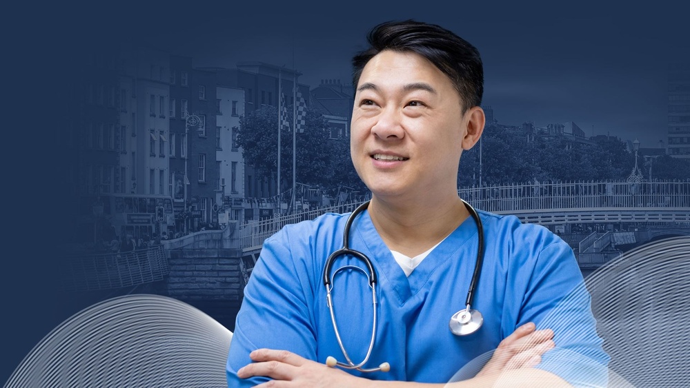 Confident doctor in blue scrubs with stethoscope, smiling in front of Ha'penny Bridge