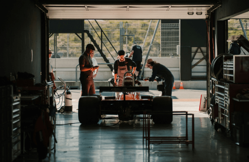 Motorsport engineers working on a single-seater race car inside a professional racing garage