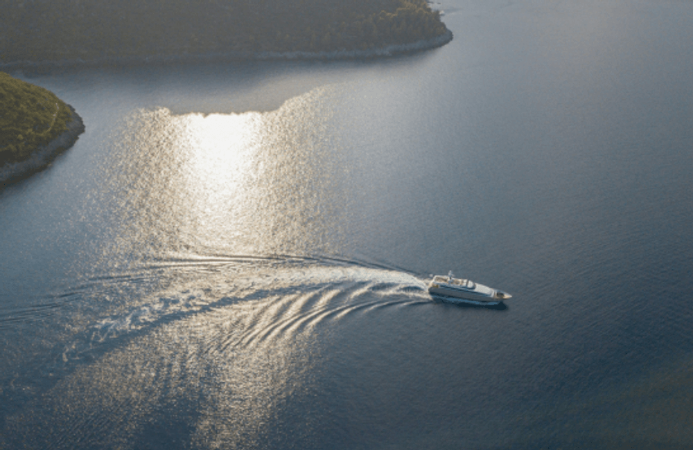 Motor yacht creating a wake while travelling through calm coastal waters at sunset.