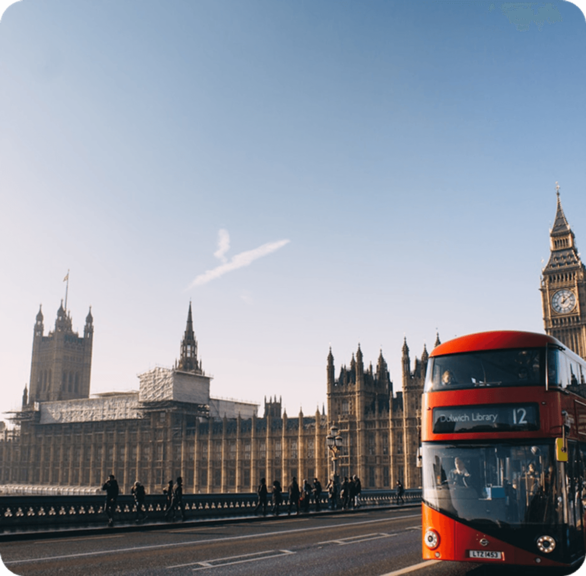 The image shows a well‑known London city scene featuring a bright blue sky and skyscraper buildings, with a red bus in front view to the right.
