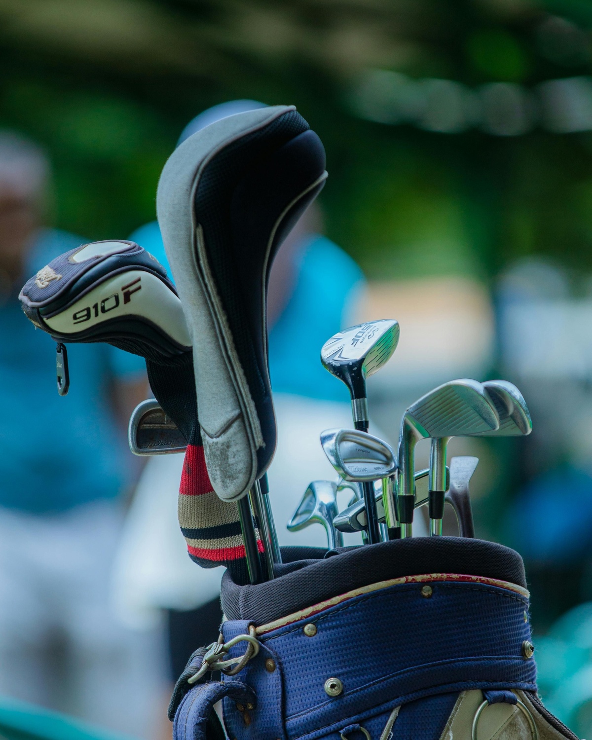 Close‑up of a golf bag filled with multiple golf clubs, including drivers and irons with headcovers, standing outdoors with a softly blurred natural background.