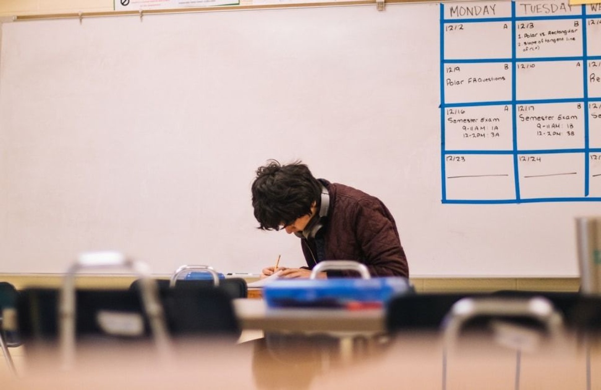The image shows a classroom or study environment with a large whiteboard taking up most of the background. The room appears quiet and academic, with a focus on individual work.