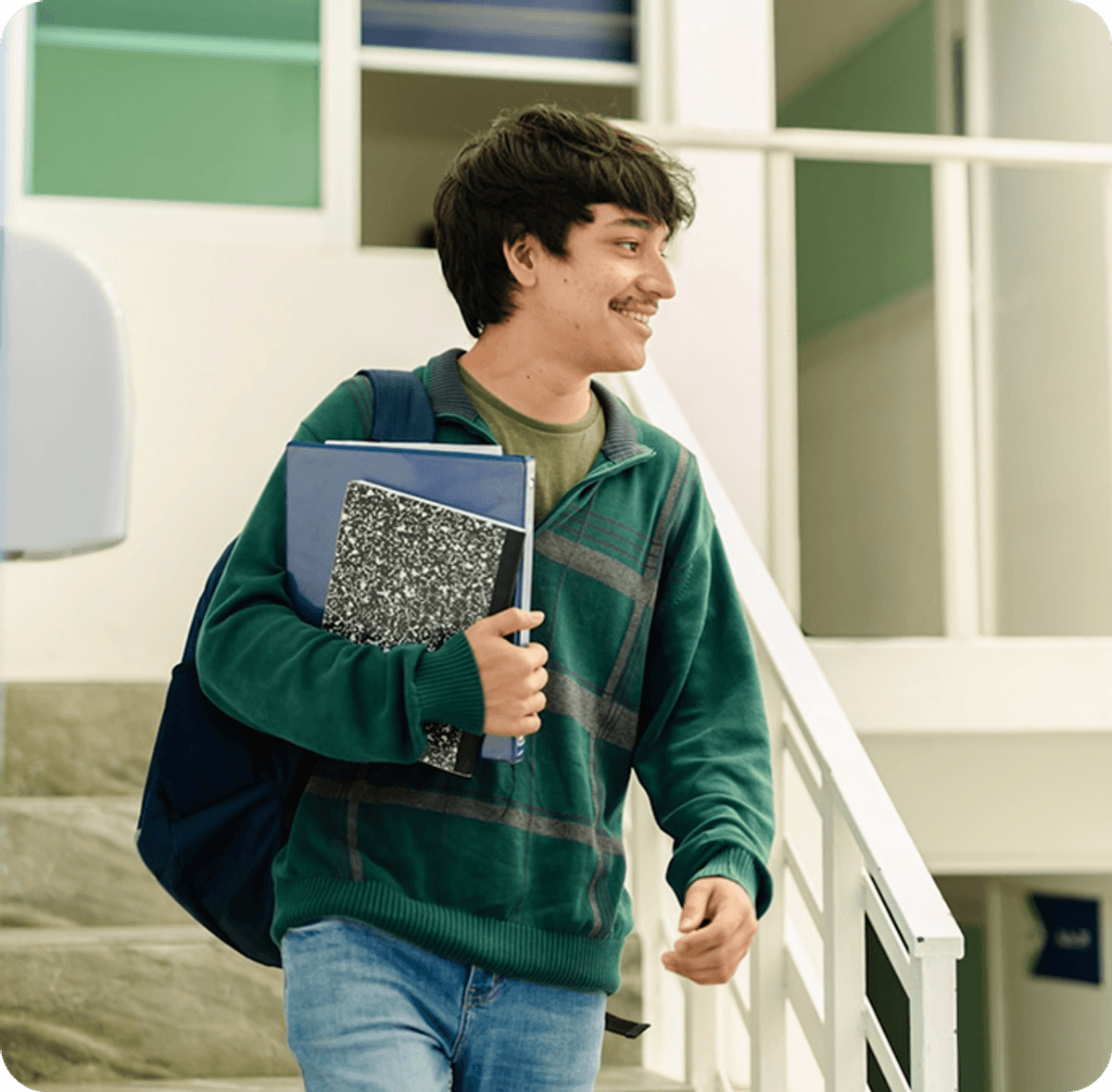 Person walking upstairs indoors, holding a notebook and wearing a backpack in a modern educational building.