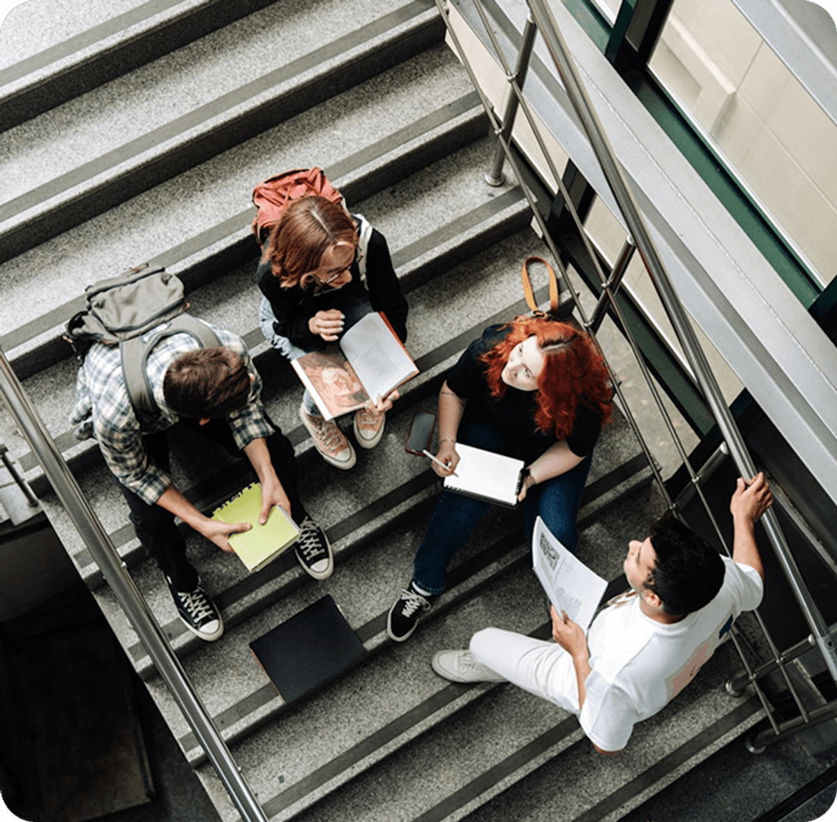 Group of people sitting on a staircase, studying together with notebooks and papers spread out around them.