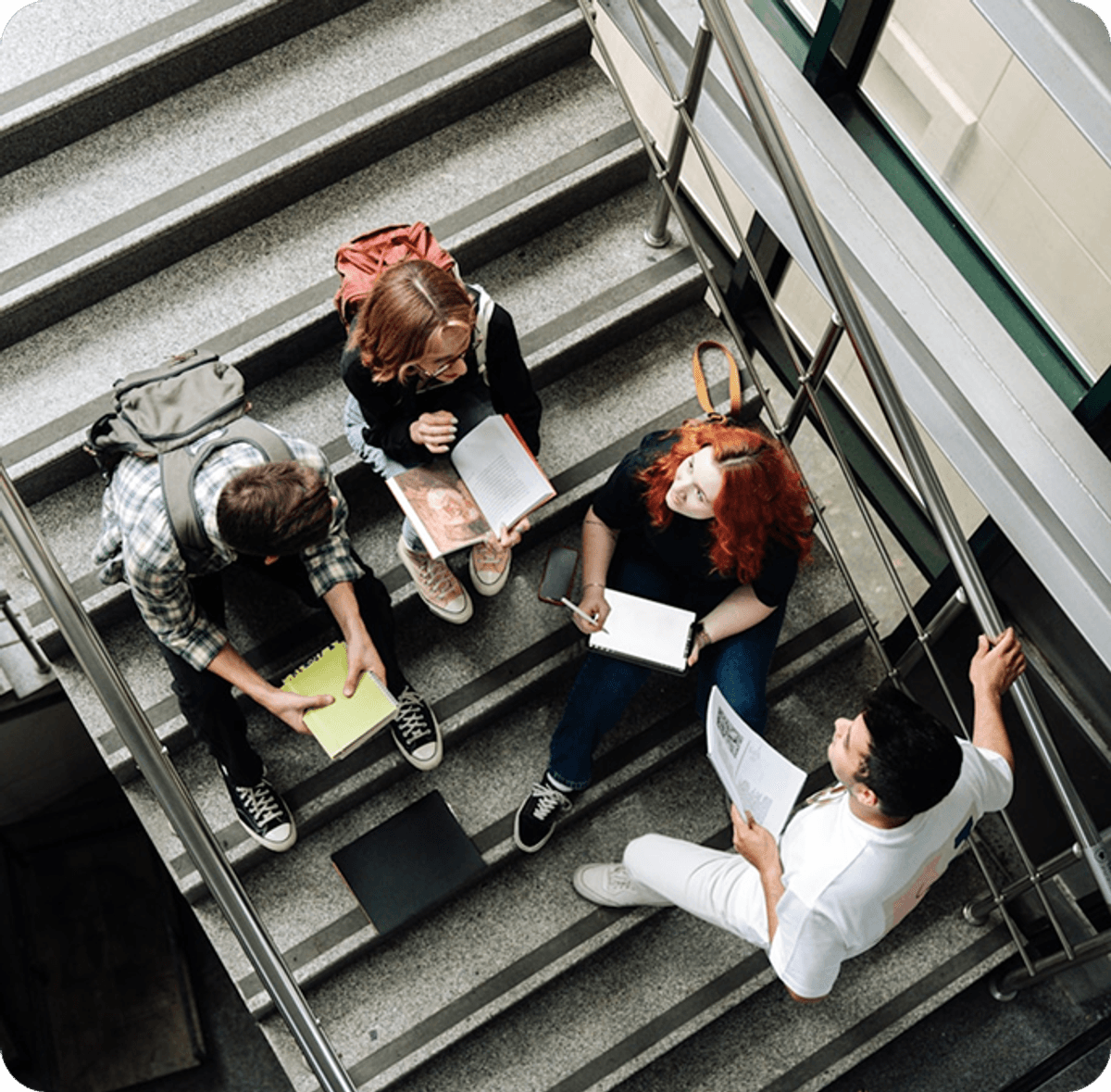 Group of people sitting together on an indoor staircase, studying with notebooks and papers spread out around them.