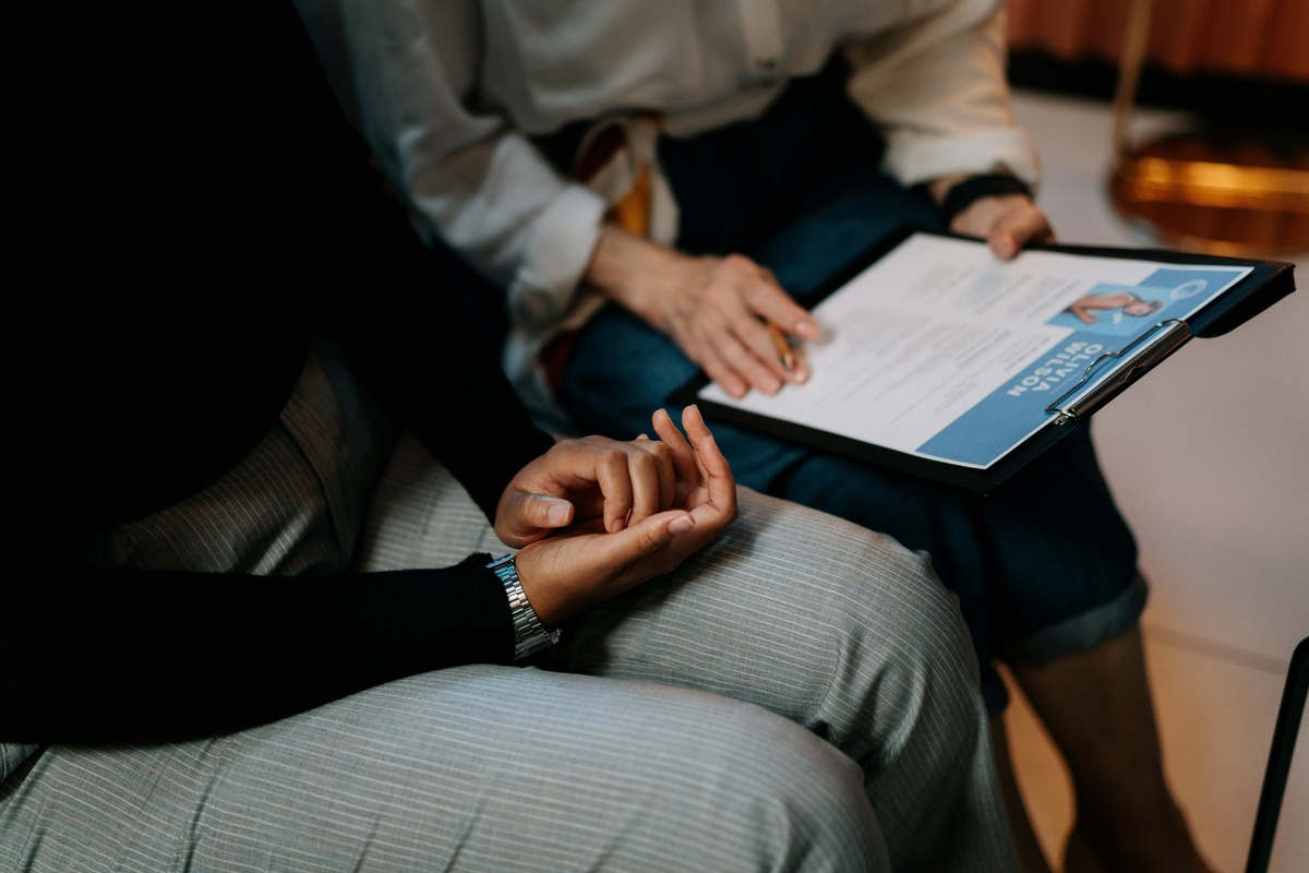 Two people sit close together while reviewing a document on a clipboard; one person holds a pen, and their hands are visible in the foreground.