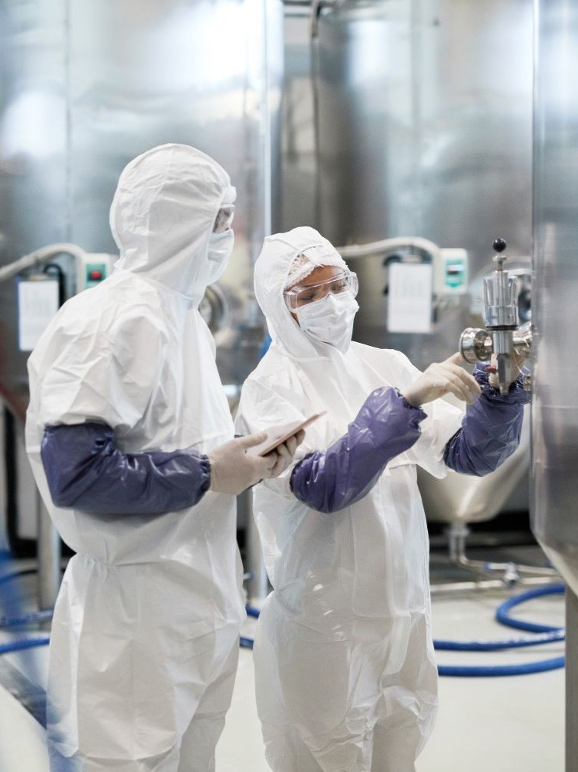 Cleanroom workers monitoring stainless-steel processing equipment in a pharmaceutical manufacturing plant