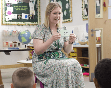Teacher holding a word card while leading a phonics or reading activity with pupils in a classroom.