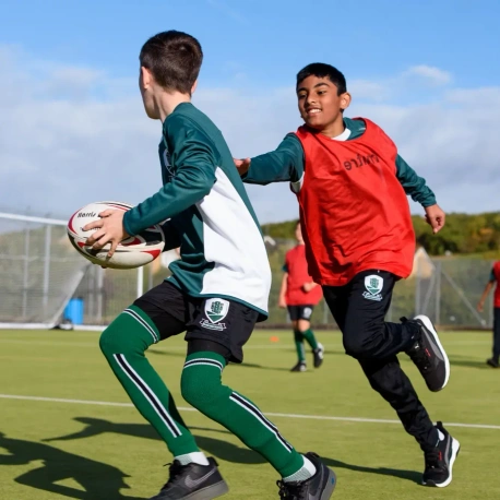 Two pupils playing rugby on a sports field, with one carrying the ball while another challenges for possession during a game.