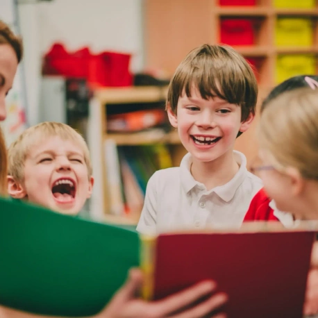 Pupils in a school reading a book and laughing.