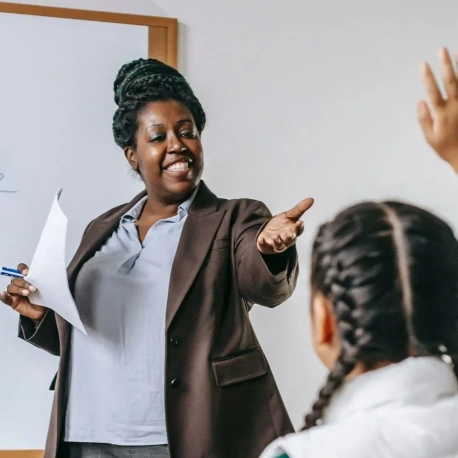 A female teacher pointing to a child with their hand raised.