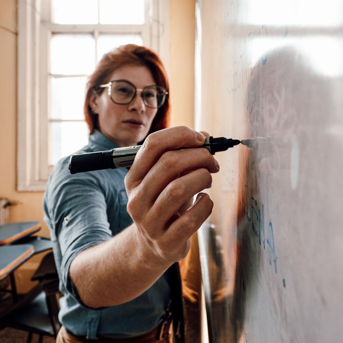 Female teacher writing on a whiteboard in a classroom.