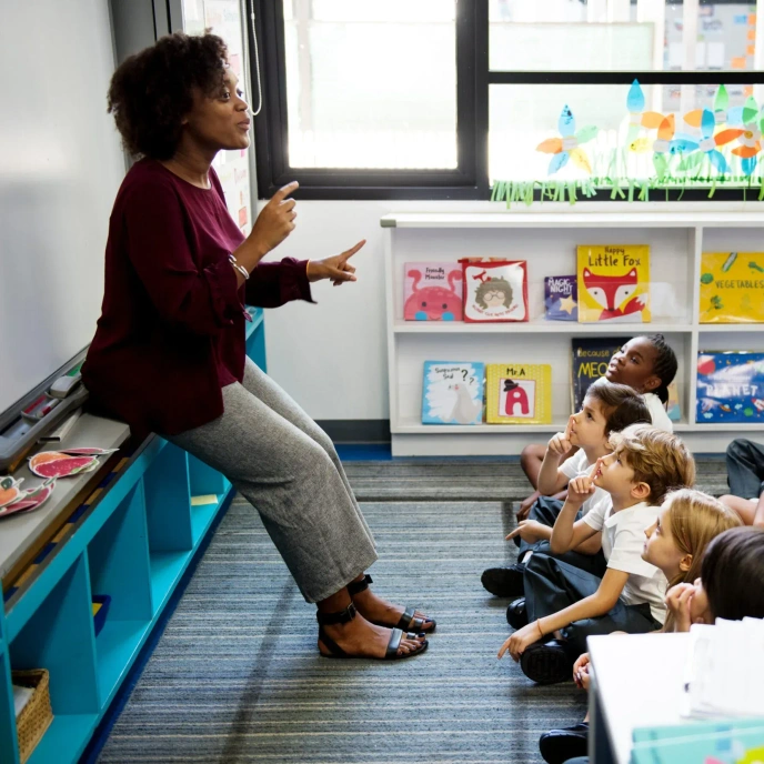 Adult leading a classroom discussion with a group of seated pupils, supporting speaking and listening skills in an early years learning environment.
