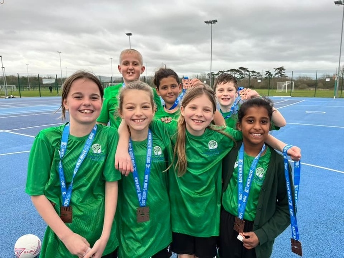 Group of pupils in green sports kits wearing medals and posing together on an outdoor sports court.
