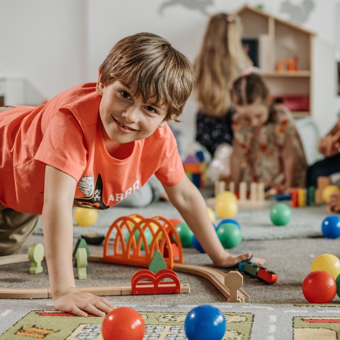 Young pupil playing with a toy railway set during an early years learning activity, with other children exploring educational toys and resources in the background.