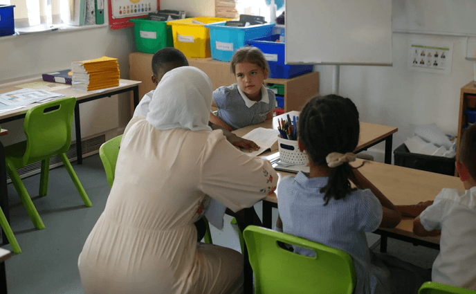 Female teacher smiling at a pupil in a classroom.