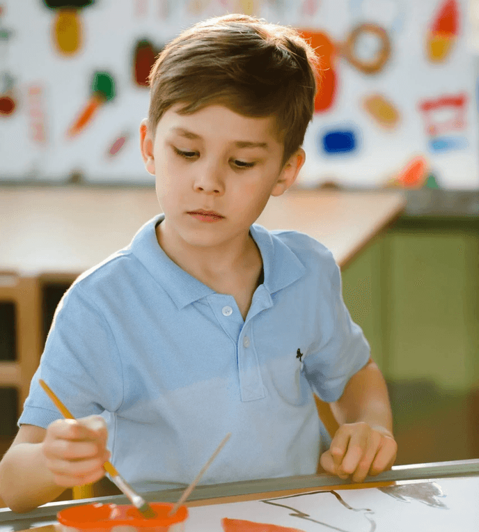 Pupil painting at a classroom table during an arts and crafts activity.
