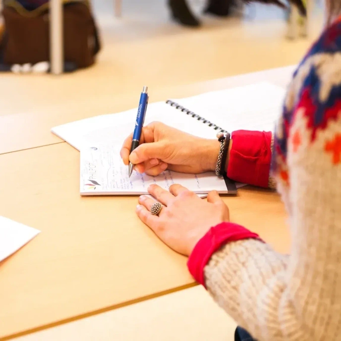 Person writing on a notepad on a desk.