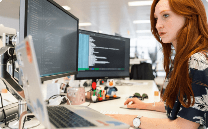 Software developer working at a desk with code on dual monitors