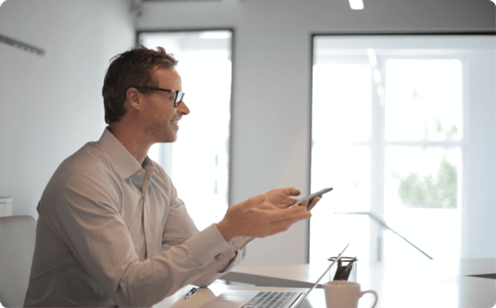 Professional in an office looking at a phone beside a laptop