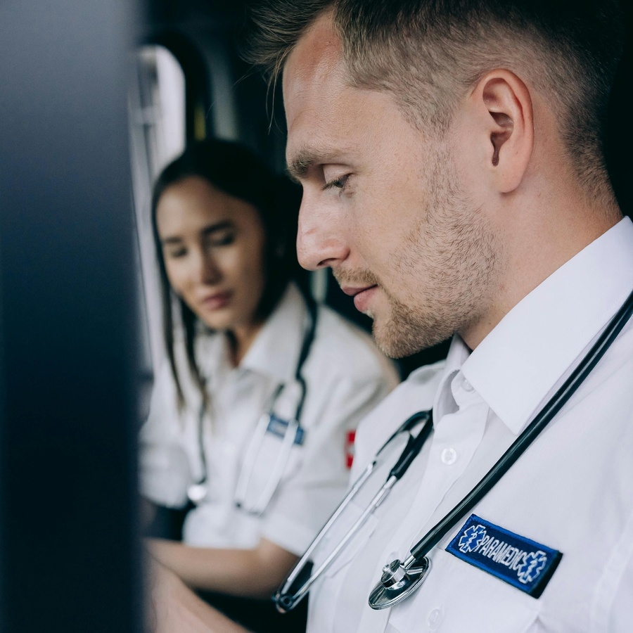 Two healthcare professionals wearing stethoscopes seated at a workstation, looking at a screen together in a clinical setting.