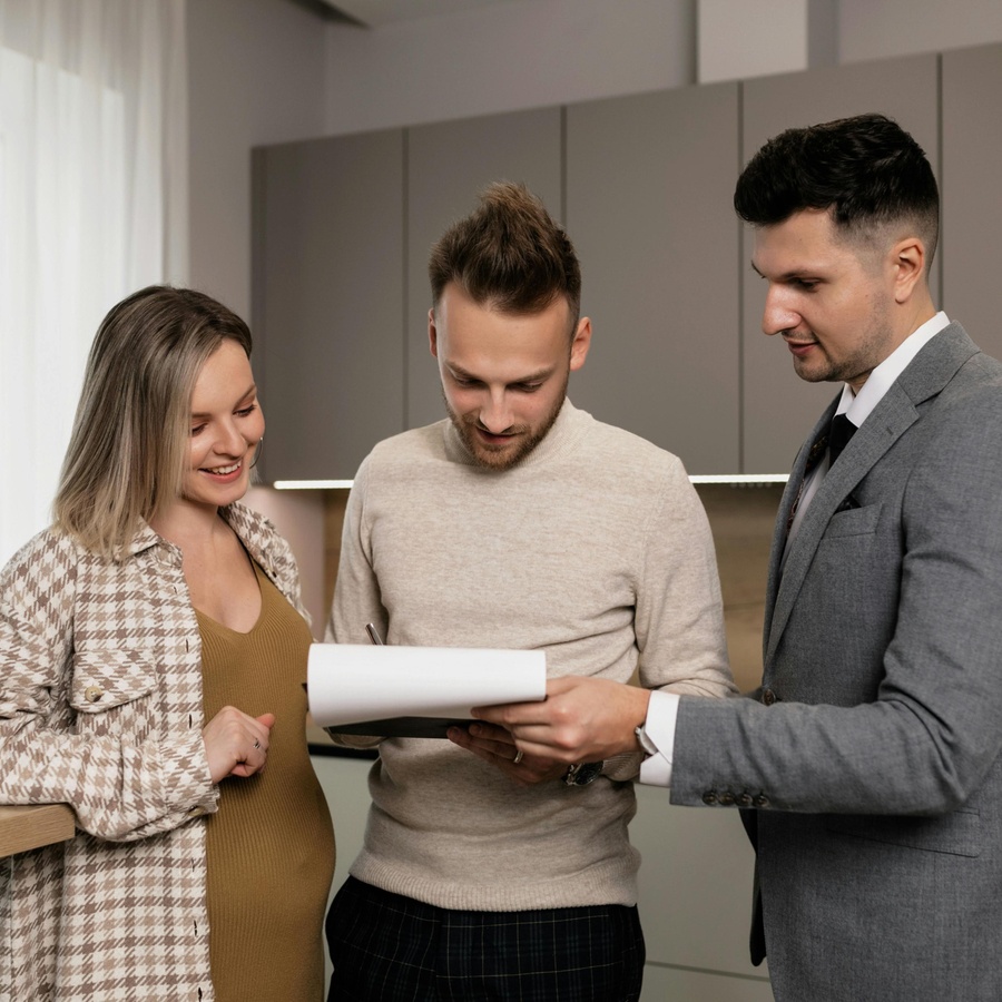 A group of three individuals standing together in a modern kitchen, looking at a document held by the individual on the right. 