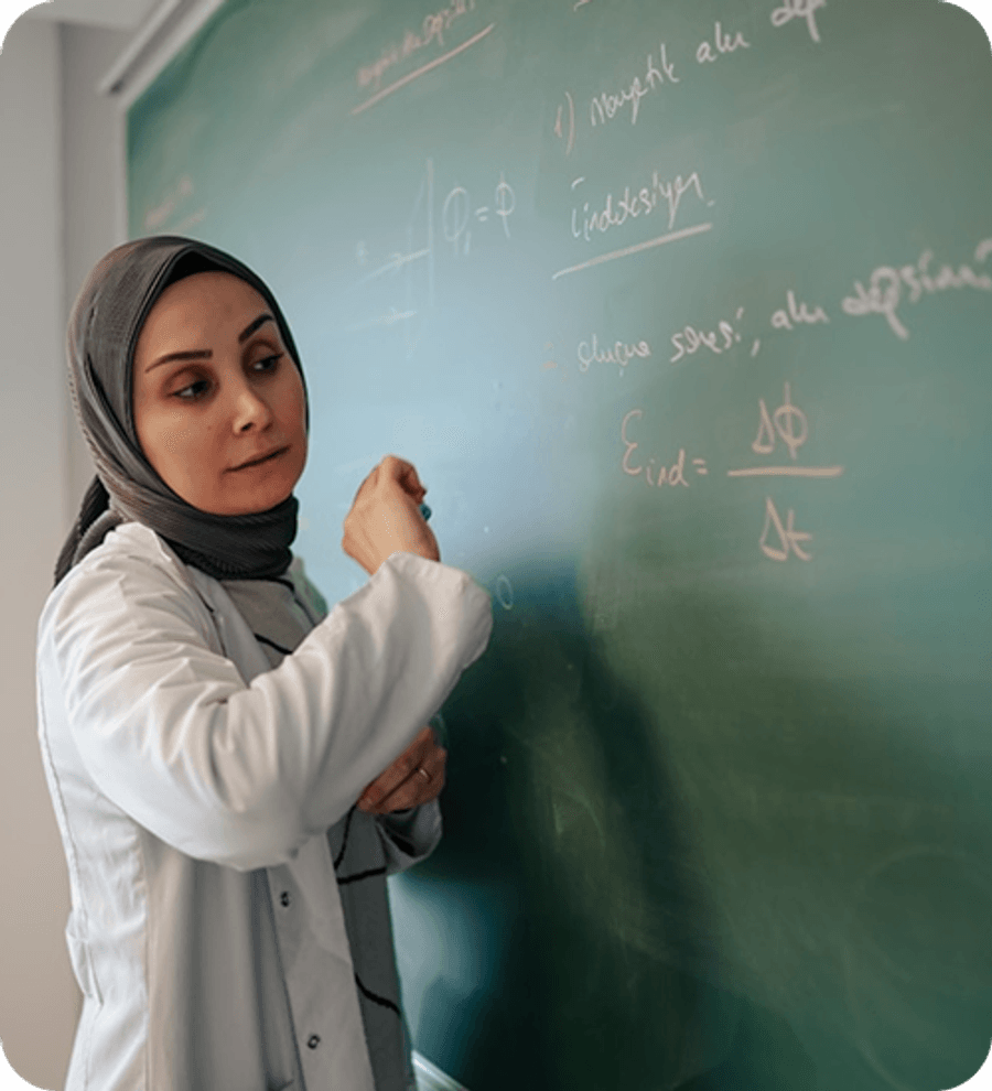 Person standing beside a chalkboard, writing mathematical equations on the board in a classroom or lecture setting.