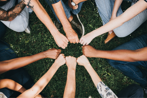 A diverse group gathers in a circle, connecting at the centre as a visual expression of teamwork, partnership, and shared purpose. The overhead perspective highlights collaboration and community, making the image ideal for content focused on inclusion, culture, and collective success.