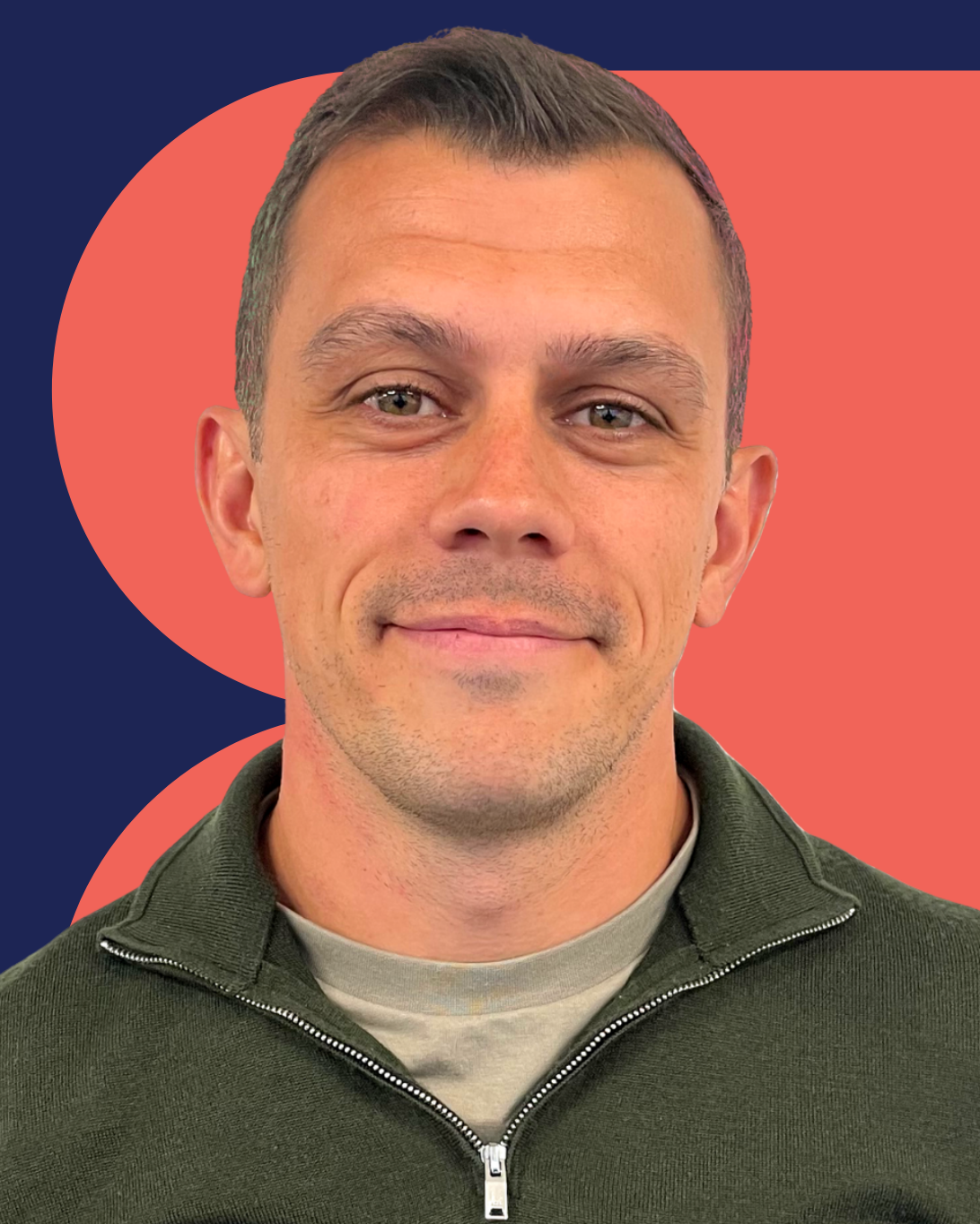 Myles Jackson smiling, wearing a green zip-up sweater, in front of a red geometric pattern.