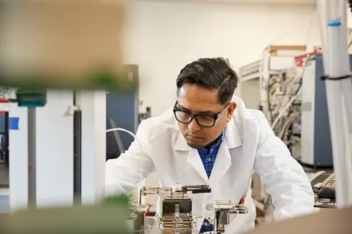 Scientist wearing a white lab coat and safety glasses conducting research in a modern laboratory, carefully operating scientific equipment as part of biotechnology, pharmaceutical, or life sciences research.