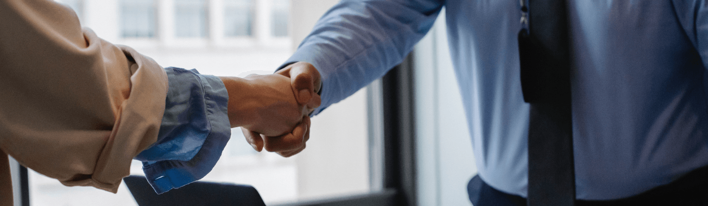 A handshake between two people above a laptop, representing partnership and mutual understanding in a business context.